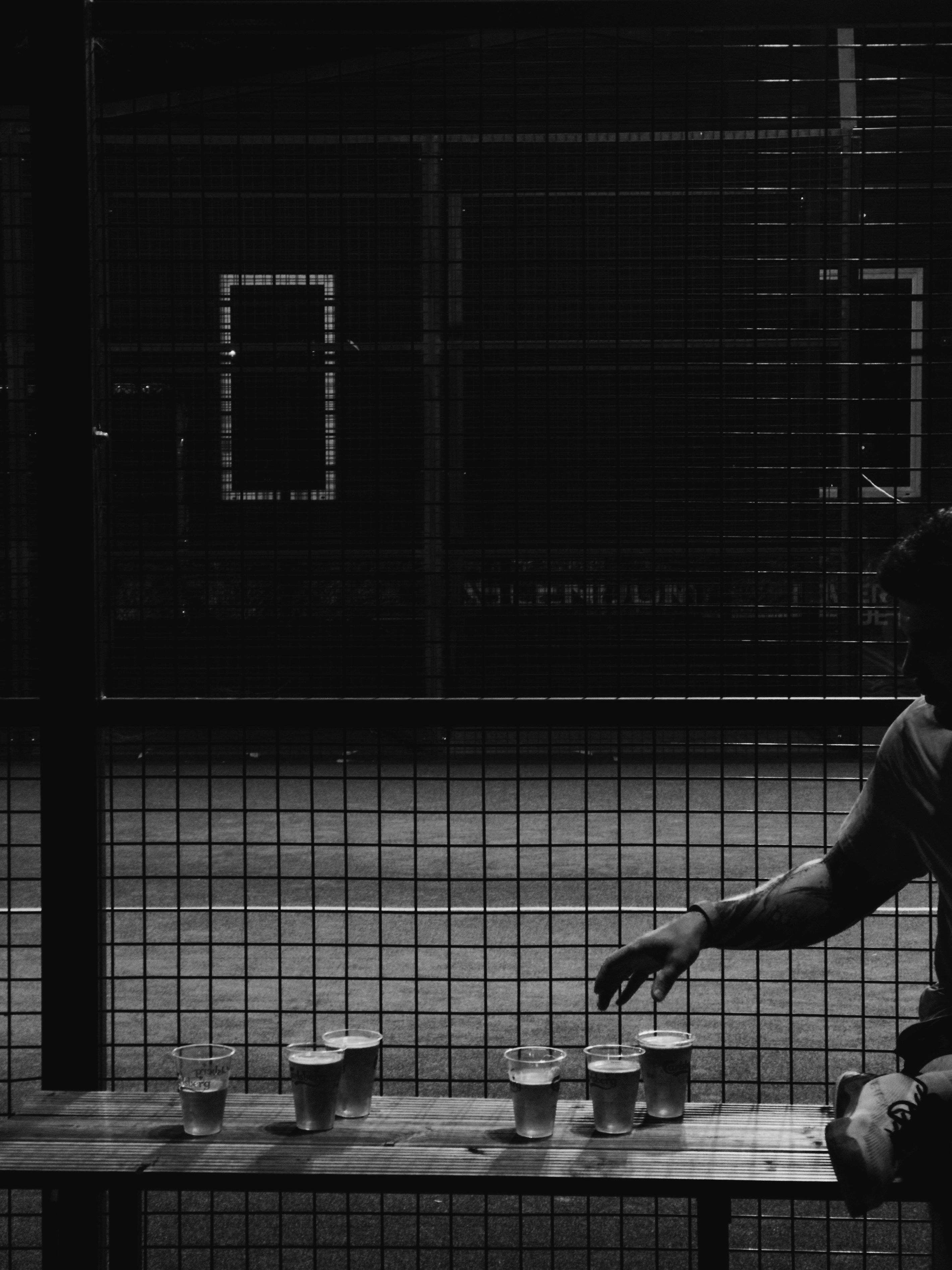 Cups of beer on a bench by the padel court, a hand reaching for one