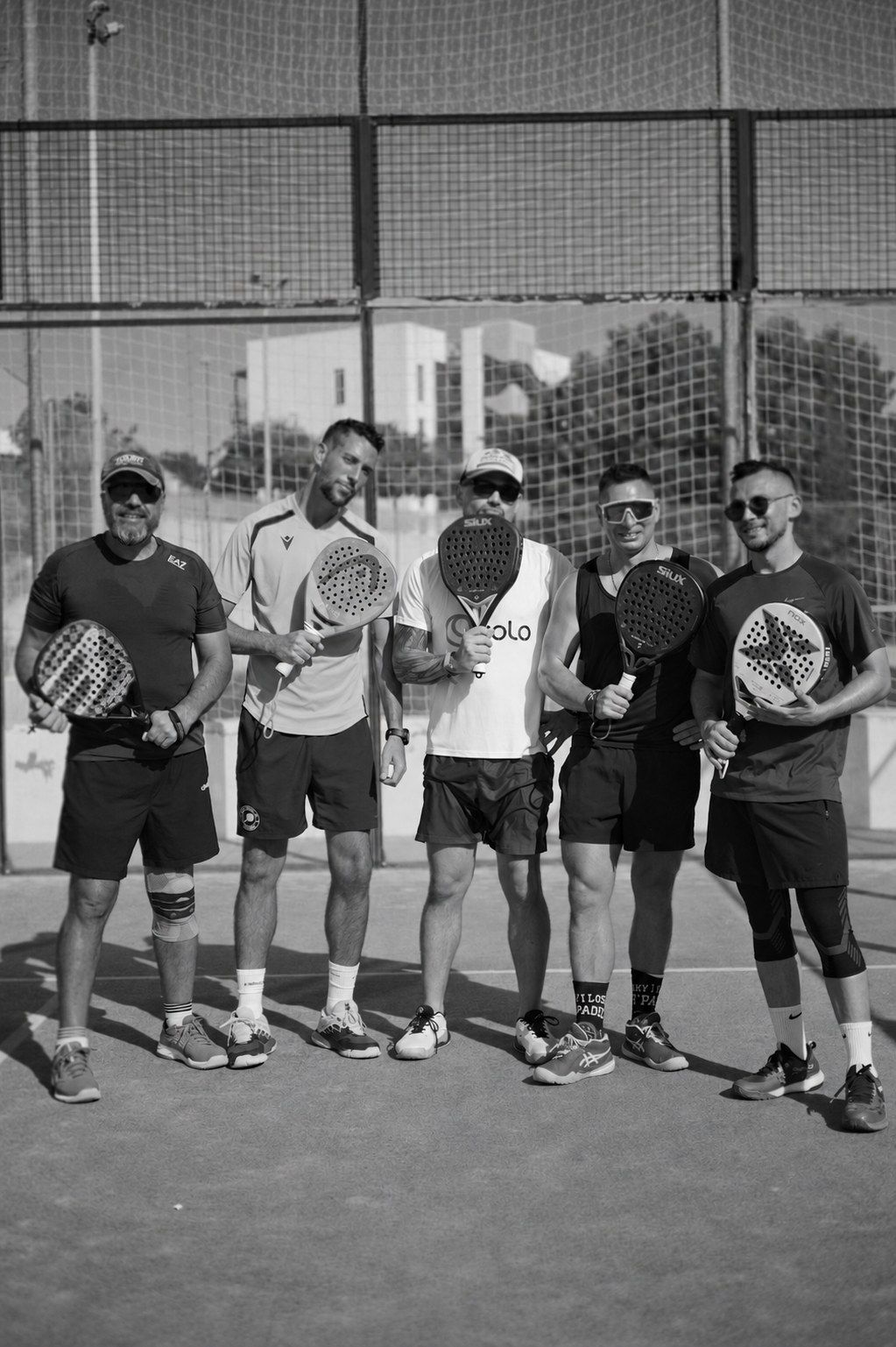 Five padel players posing with their rackets on the court